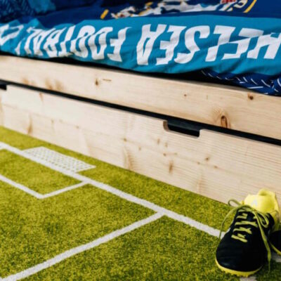 Drewniane łóżko bramka z wysuwaną szufladą na tle dywanu boiska i butów piłkarskich