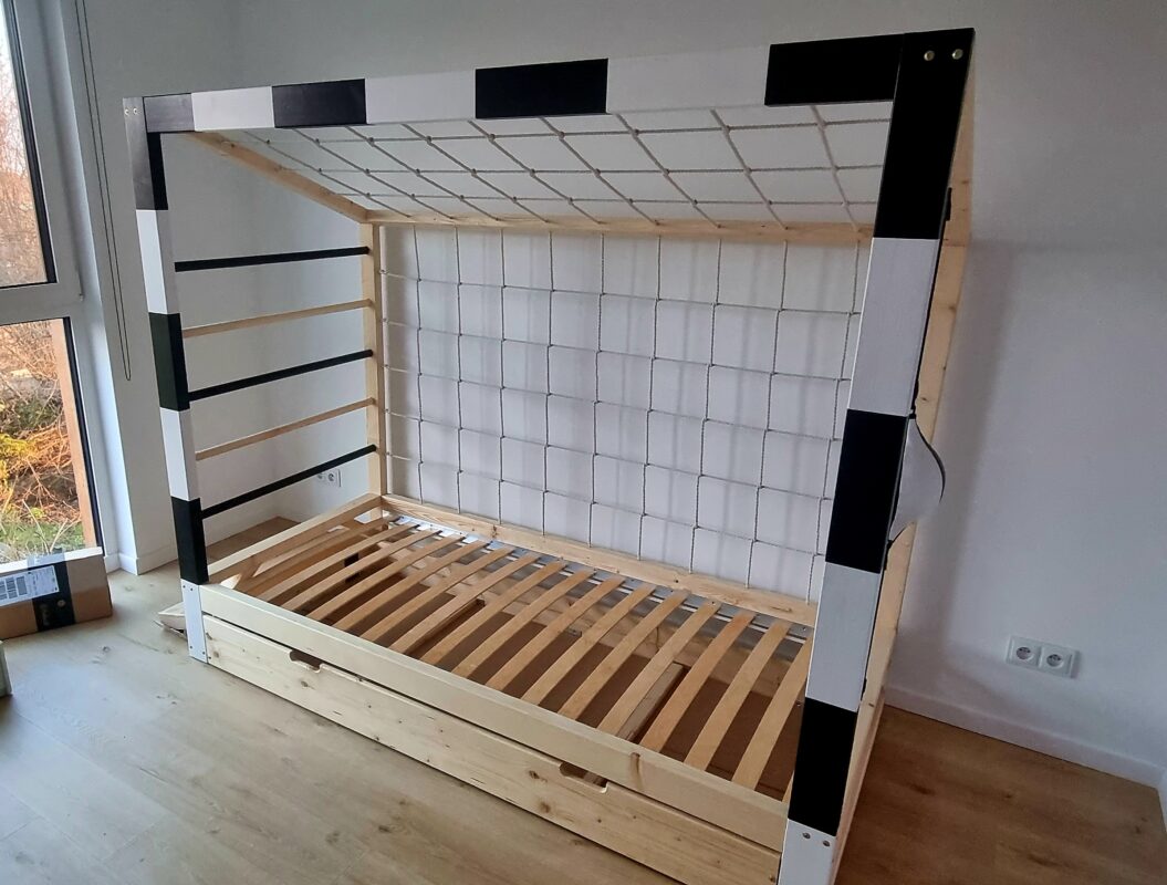 Łóżko bramka piłkarska Paco Design z drewnianą ramą i siatką, podczas montażu w pokoju dziecięcym