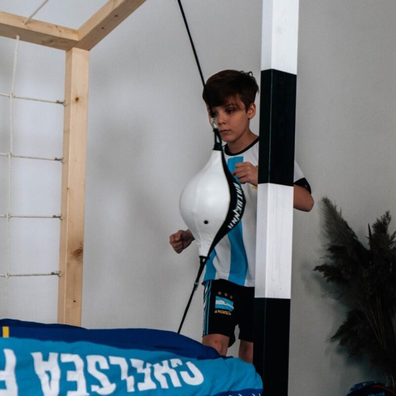 Chłopiec obok łóżka bramki piłkarskiej Paco Design uderzający w worek treningowy