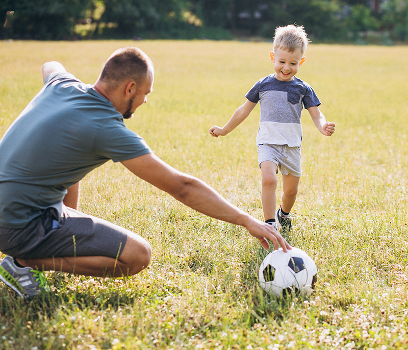 Ojciec bawiący się piłką nożną z małym synem na łące