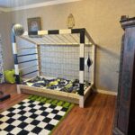 Łóżko dziecięce w kształcie bramki piłkarskiej Paco Design w pokoju z drewnianą podłogą i sportowymi dekoracjami