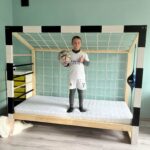 Dziecko w stroju piłkarskim stojące na łóżku bramce Paco Design w pokoju dziecięcym